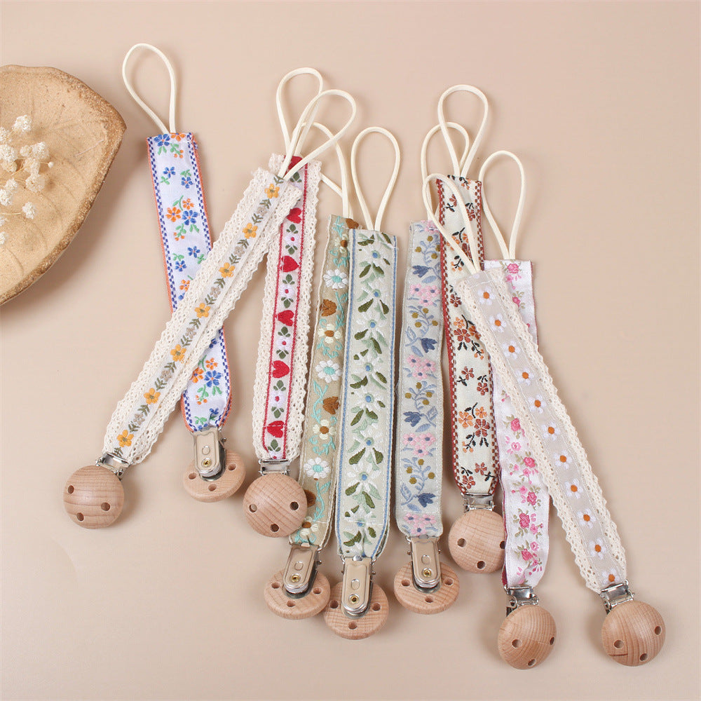 Beech Wood Dummy Clip, Embroidered Soother Holder, shown on a bed