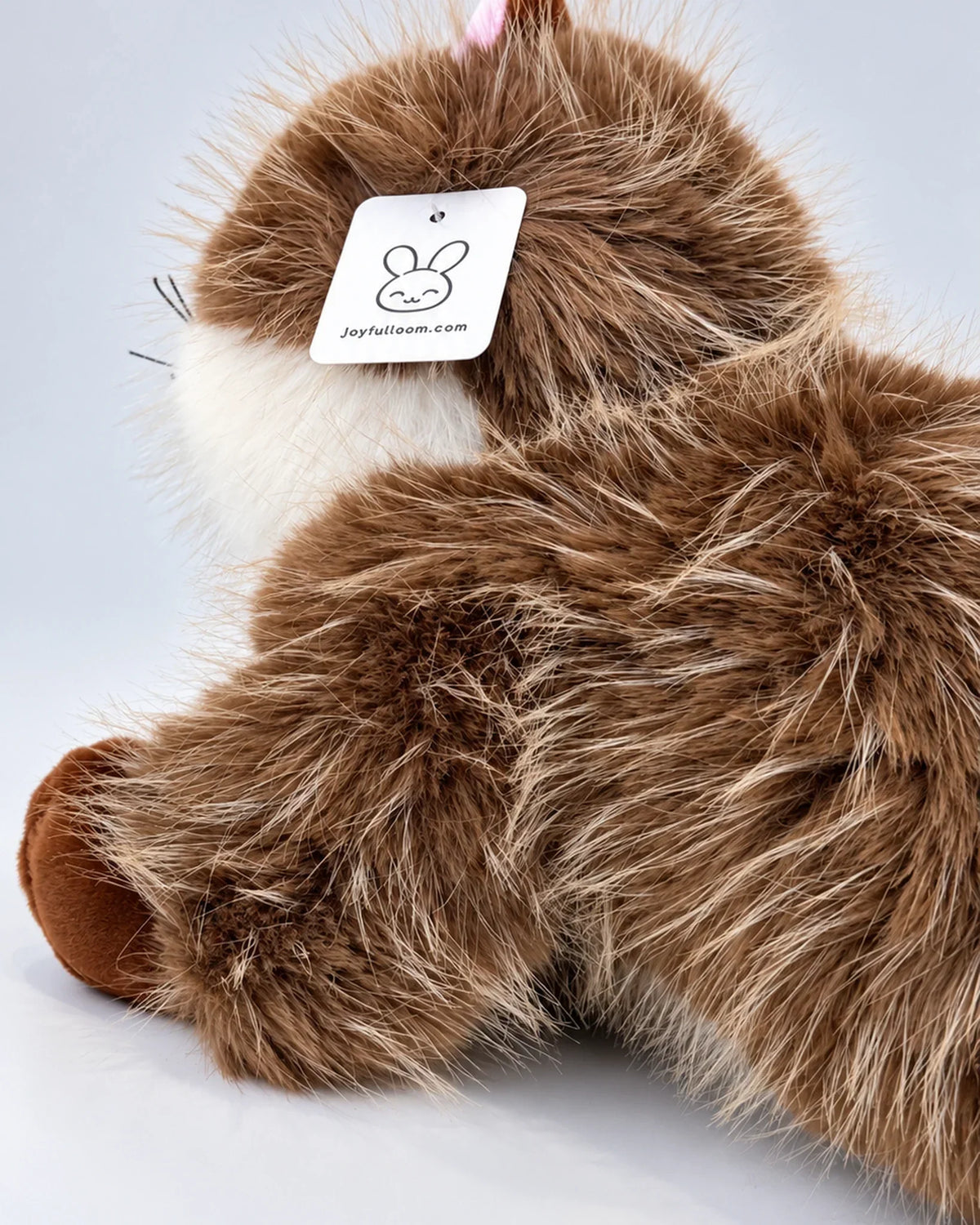 Realistic brown and white Ragdoll-style cat plush toy, lying down, back view